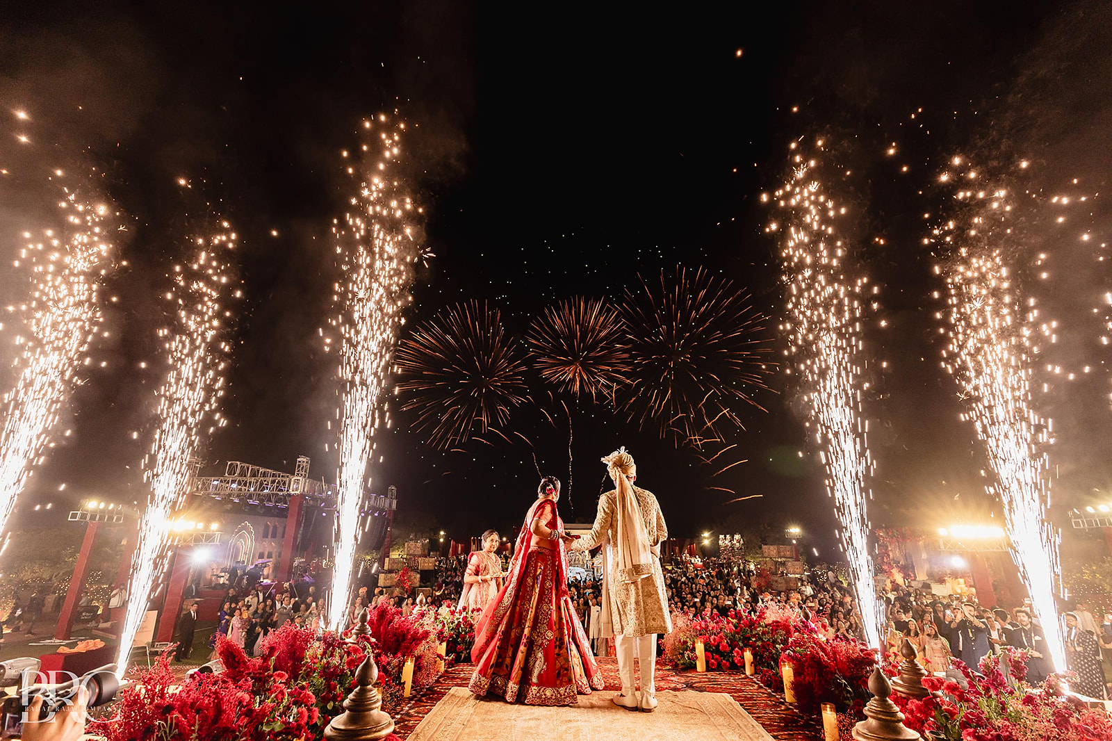 The couple on stage beneath fireworks and sparkler fountains